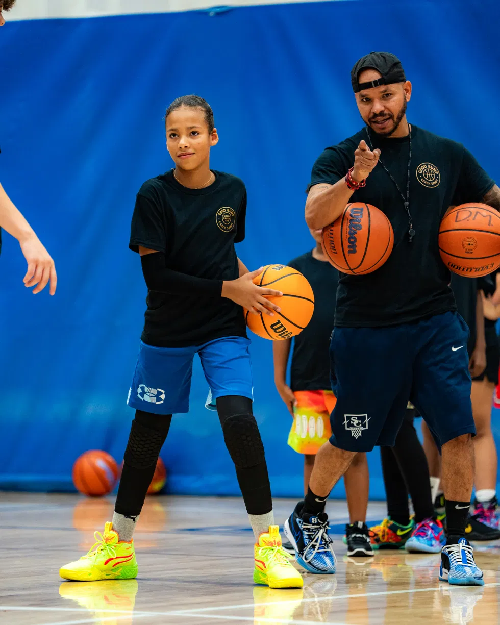Coach Sandy handing a basketball to a young player during instruction